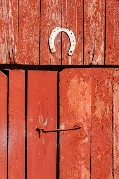 A weathered barn door painted red, featuring a brass horseshoe hung above a rustic latch, reflecting a charming rural atmosphere.