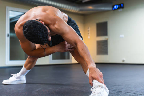 A young man engages in a strength training routine in a gym, showcasing his dedication to fitness and active lifestyle. He is practicing a stretching exercise to enhance flexibility.