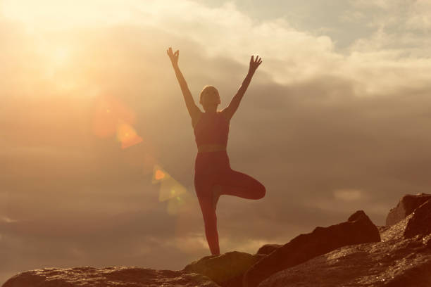 istock woman doing a tree pose yoga position outdoors on rocks at sunrise, sunset. 2167173627