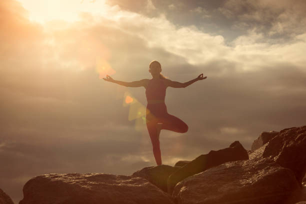 istock woman doing a tree pose yoga position outdoors on rocks at sunrise, sunset. 2167173630