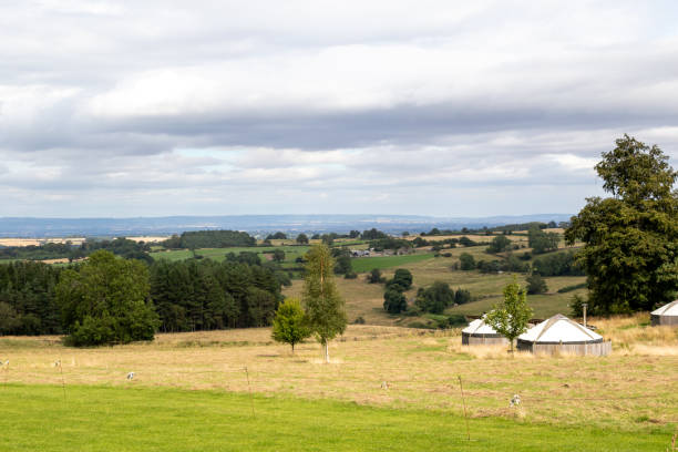 Rural landscape with yurts, rolling hills, and scattered trees under a cloudy sky in Yorkshire Dales, England.