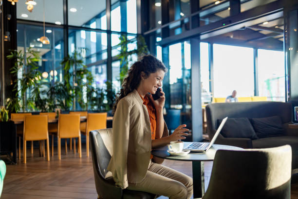 Woman on phone with laptop in modern cafe setting