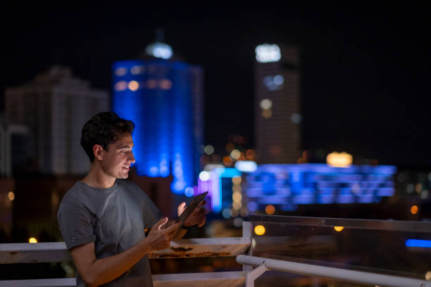 Young man using digital tablet at night with city in the background