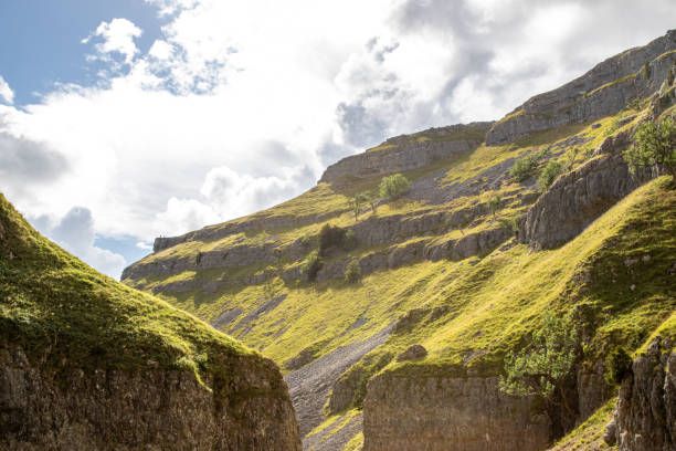 istock Scenic view of sunlit green hills with rocky cliffs under a cloudy sky. 2167197264