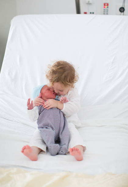 Siblings meet newborn baby in hospital. Child holding new infant brother for the first time. Kids visit mother in labor and delivery ward after birth of new baby. Sibling love. Family bonding.