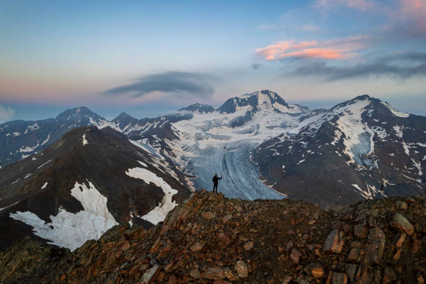 Hiker on top of a mountain taking photos with the smartphone at snowy peaks at dusk, Palla Bianca (Weißkugel), Hintereisferner glacier, Otzal Alps (Otzi Alps), Tyrol, Austria, Europe