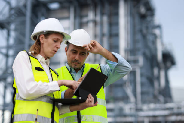istock Senior man and woman engineer wearing green reflective vest and white hardhat work discussing on a laptop at the site power plant 2167204010