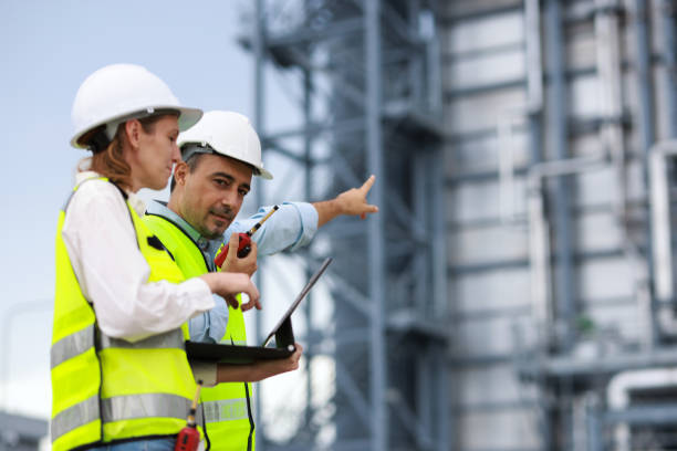 istock Senior man and woman engineer wearing green reflective vest and white hardhat work discussing on a laptop at the site power plant 2167204011