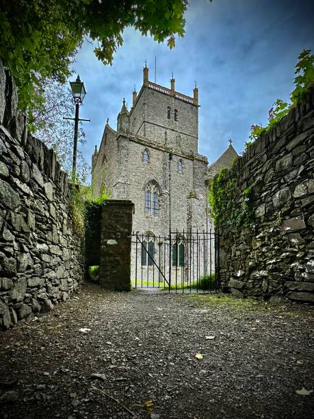a black wrought iron gate behind st davids cathedral (eglwys gadeiriol tyddewi) in pembrokeshire, yields access from an ivy-covered stone footpath