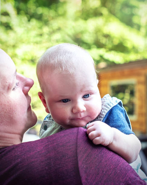 istock Mother cradles three-month-old infant in serene Poconos forest. Parent comforts light-haired, blue-eyed baby. 2167211390