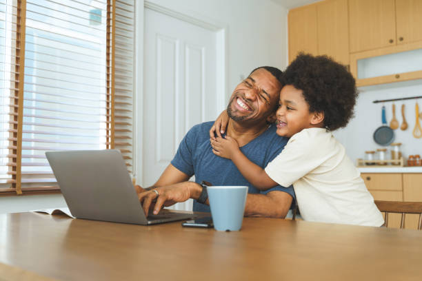 istock Black African American Father and son sharing a loving hug at kitchen table while working on laptop, illustrating affection and family bonding. 2167211824