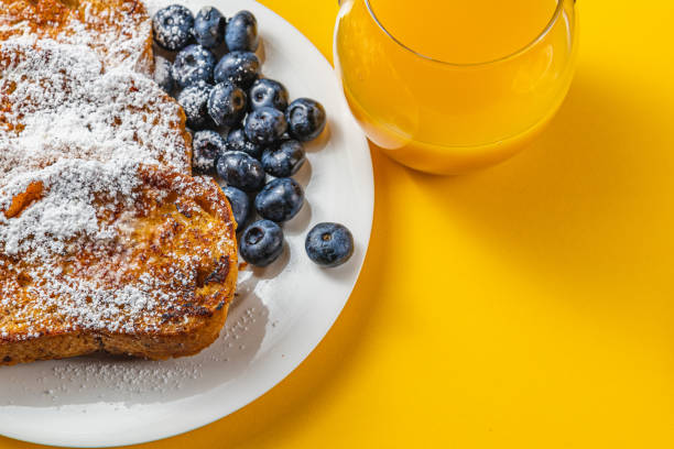 French toast on a white plate with blueberries and orange juice for breakfast