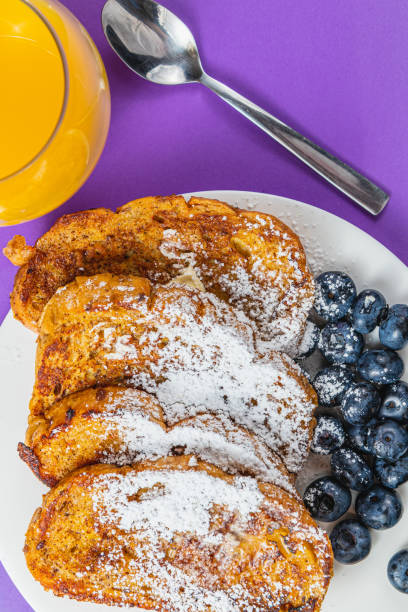French toast on a white plate with blueberries and orange juice for breakfast