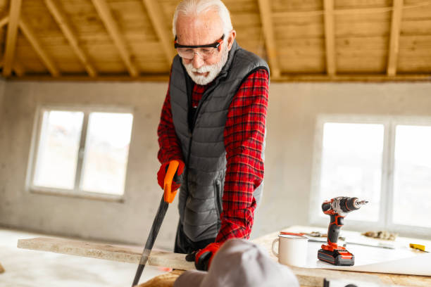 Senior carpenter working at his workshop sawing plank with hand saw