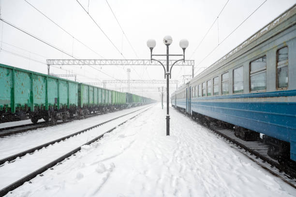 Train station peron covered by snow in winter time. Passenger train and freight wagons on snowy railways. Ukraine, Europe