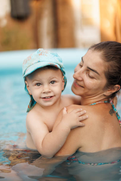 Young mother hugging her baby son in wading pool on sunny day