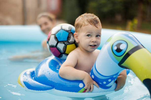 Happy baby boy floating in inflatable swim ring while cooling off with his mother in wading pool on sunny day