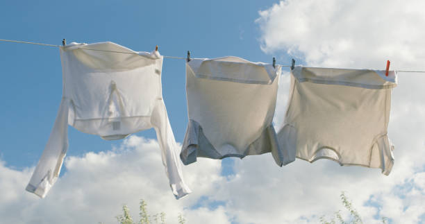 istock Three white shirts sway on a clothesline under a clear sky with soft clouds. 2167238730