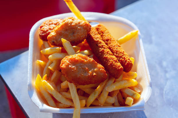 Styrofoam container with a variety of fried foods including chicken, french fries, and a doughnut. Fries alongside a crispy piece of chicken, ready to be enjoyed