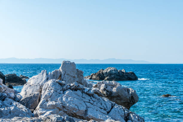 A serene coastal scene featuring rugged, white rocky formations against a backdrop of calm blue ocean. The contrast between the rough texture of the rocks and the smooth surface of the sea creates a tranquil yet striking visual, capturing the natural beauty of coastal landscapes.