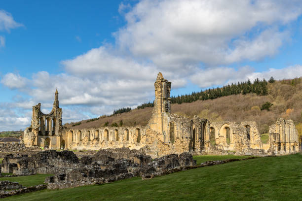 istock Scenic view of ancient abbey ruins under a blue sky with clouds, surrounded by green fields and hills at Byland Abbey 2167254638