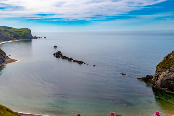 Serene coastal landscape with cliffs, calm blue sea, and wispy clouds in a clear sky at Durdle Door, England.
