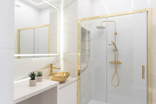 istock Home interior with ceramic bathroom sink on cupboard with gold water tap and shower with tile on the wall with marbled effect.  Interior decor. 2167256123