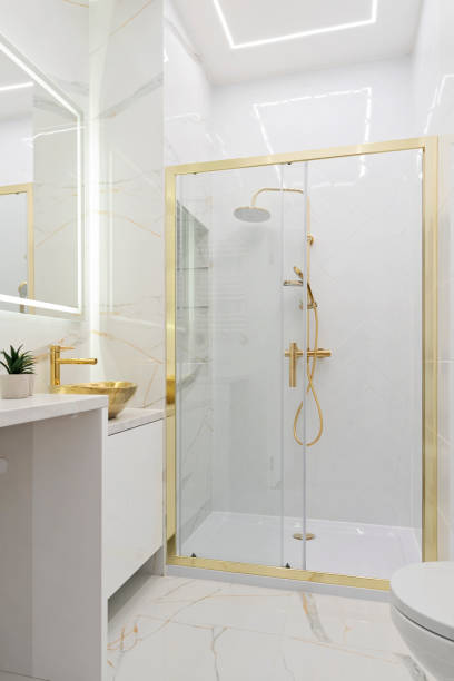 istock Home interior with ceramic bathroom sink on cupboard with gold water tap and shower with tile on the wall with marbled effect.  Interior decor. Vertical. 2167256132