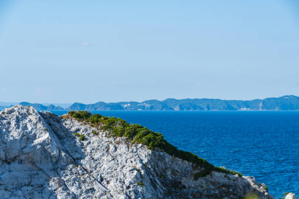 This image captures the contrast between rugged white rocks in the foreground and the calm, deep blue ocean extending to a distant line of islands. The clarity of the sky and the vibrant colors enhance the scene's natural beauty, creating a tranquil atmosphere.