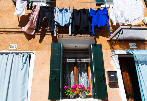 Burano, Italy-April 25, 2024: Brightly colored laundry hanging on a line above a vibrant window with flowers in Burano, Italy.