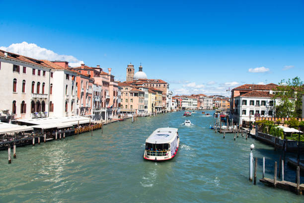 Venice, Italy-April 25, 2024: A water bus cruises along the bustling Grand Canal in Venice, Italy, surrounded by colorful historic buildings under a clear blue sky.