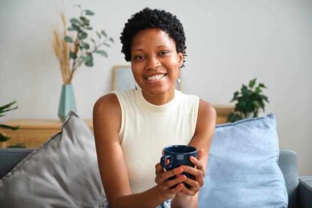 istock Young mixed race woman smiling and holding a mug while sitting on sofa 2167269497