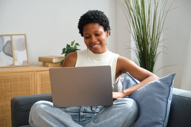 istock Young mixed race woman using laptop while relaxing on sofa at home 2167269822