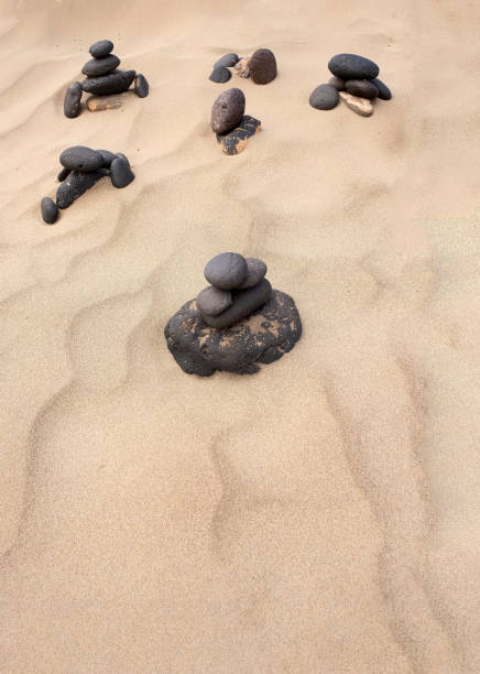 rounded stones arranged on a tranquil sandy beach, with soft natural patterns formed by the wind in the sand, representing concepts of balance, harmony, copy space, beach texture, vertical