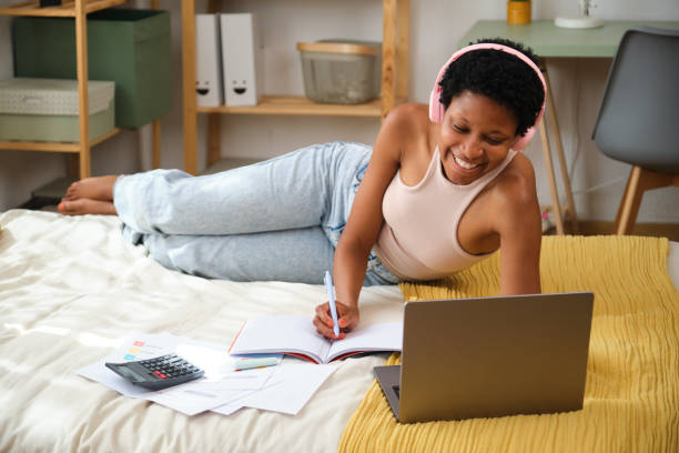 istock Young black woman lying on bed working remotely from home office 2167273885