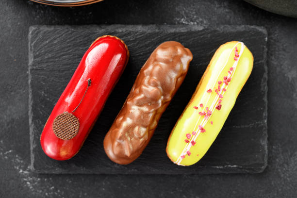 Set of beautiful french eclairs with different colorful toppings on black background, top view
