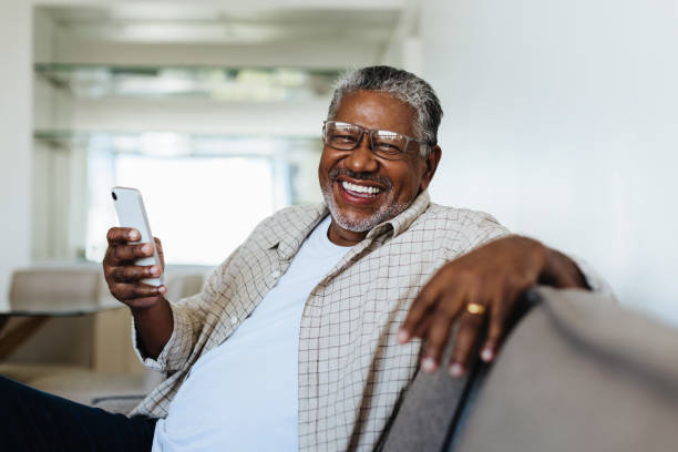 cheerful man using technology at home, smiling and relaxing on the couch - gladlynt bildbanksfoton och bilder