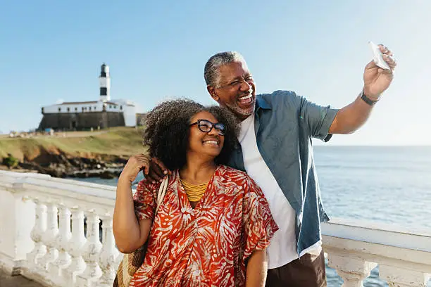 Modern Retirement: Elderly couple taking a selfie at the seaside with a lighthouse in the background Modern Retirement: Elderly couple taking a selfie at the seaside with a lighthouse in the background