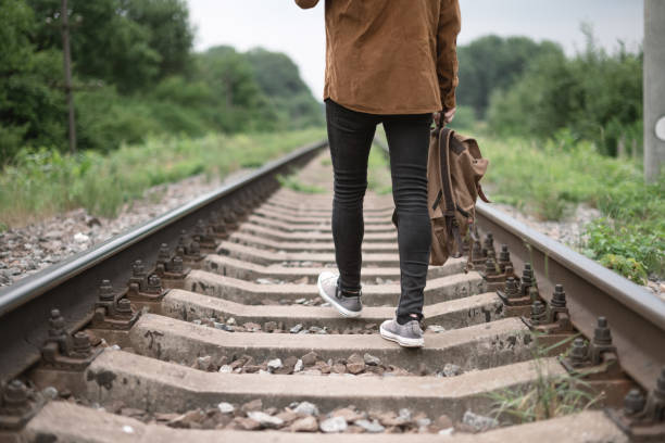 Hipster teen in black jeans pants and grey sneakers with backpack on railway. Travel concept