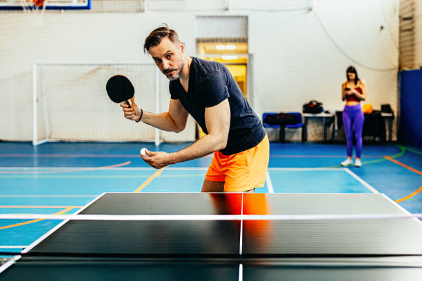 istock Close-up of a determined player getting ready to serve in a competitive table tennis match, with a vibrant orange ball and racket in a well-lit indoor sports arena 2167282576