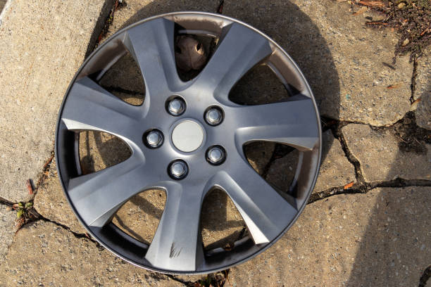 Silver car wheel hubcap resting on concrete ground - sunlight casting shadows. Taken in Toronto, Canada.