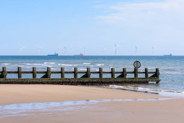 Offshore wind farm off the coast of Scotland on a clear summer day. A groyne on a sand beach at low tide is in foreground.. Aberdeen, Scotland, UK.