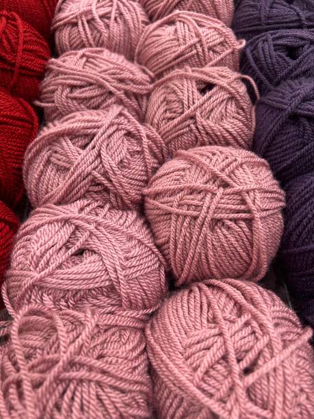 The image showcases neatly arranged balls of yarn in varying shades of pink, deep red, and dark purple. The yarns are tightly wound, highlighting their soft and smooth texture, perfect for knitting or crocheting projects. The color arrangement creates a visually appealing gradient, with the warm tones transitioning from soft pinks to bold reds and deep purples, suggesting a range of creative possibilities for textile crafting.