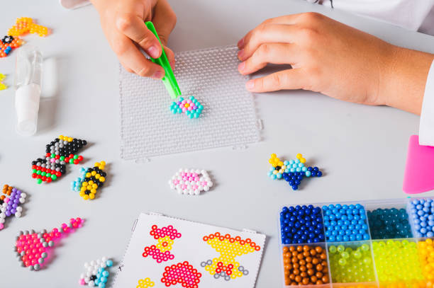 istock A girl makes a pattern of aqua beads using tweezers on a pegboard 2167306963