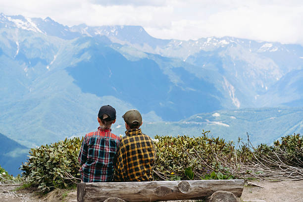children sitting on log bench observing beautiful mountains view. High quality photo