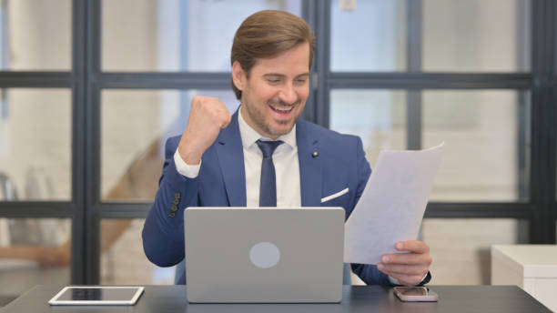 istock Excited Young Businessman Celebrating Success while Multi Tasking at Work 2167316791