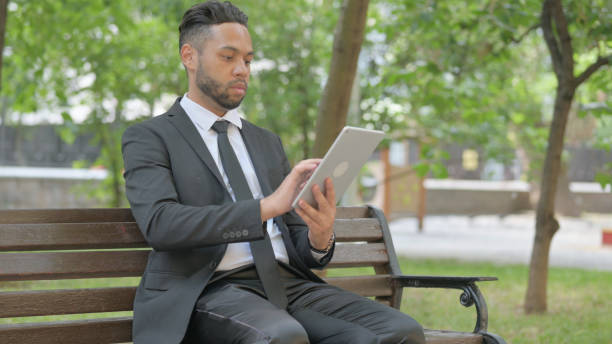 istock Mixed Race Businessman Using Digital Tablet while Sitting Outdoor 2167321927