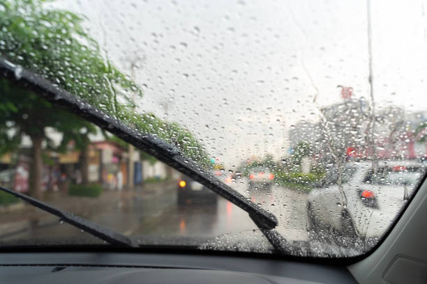 Car windshield with rain drops and frameless wiper blade closeup.