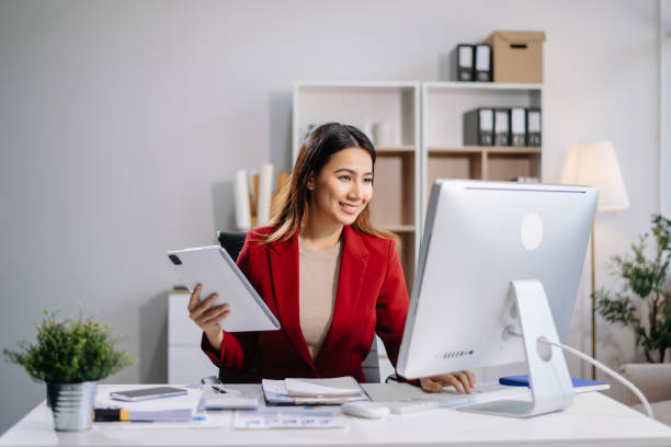 istock Young beautiful woman typing on tablet and laptop while sitting at the working white table in modern office 2167342532