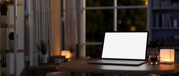 istock A laptop computer on a table in a room at home at night, illuminated by a table lamp. 2167345730